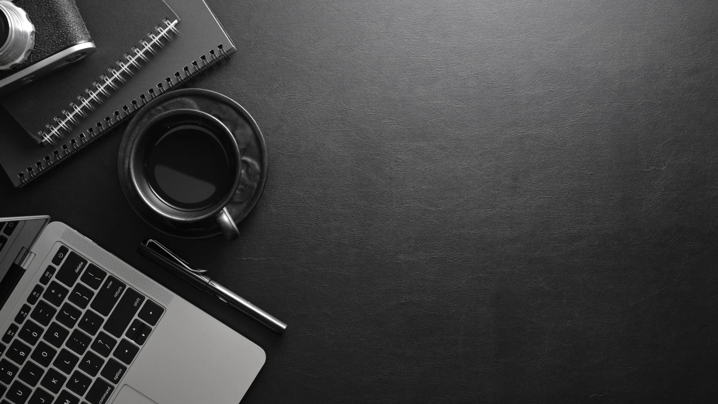 Professional workspace with notebooks, a laptop, camera, pen, and coffee